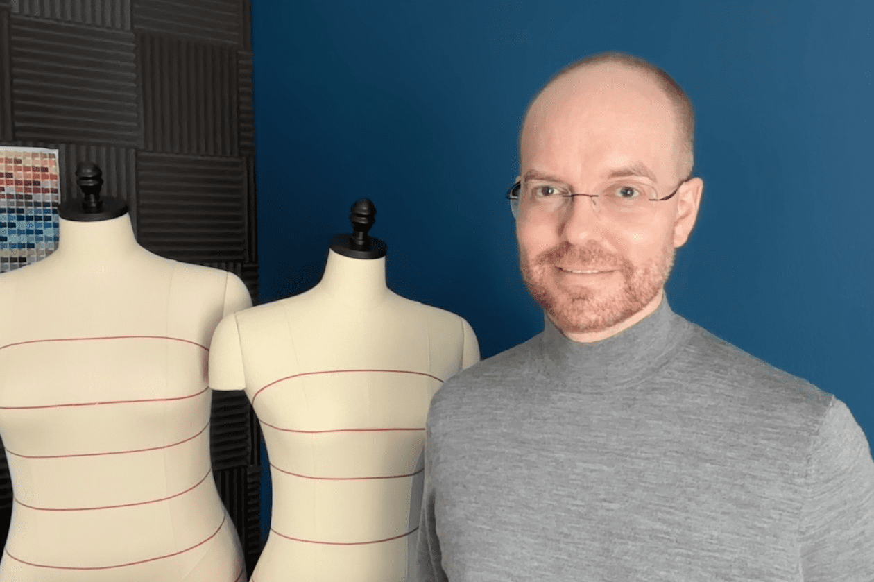 Eric Bunner-Sorg standing next to two dress forms on a background composed of a blue wall and black foam acoustic panels with a color chart